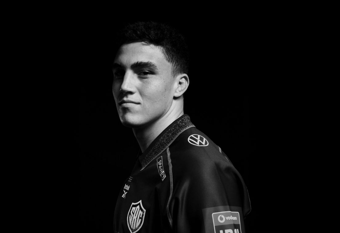 Black and white studio portrait of Matt Romao in the Sharks jersey, looking back over his shoulder at the camera against a black background.