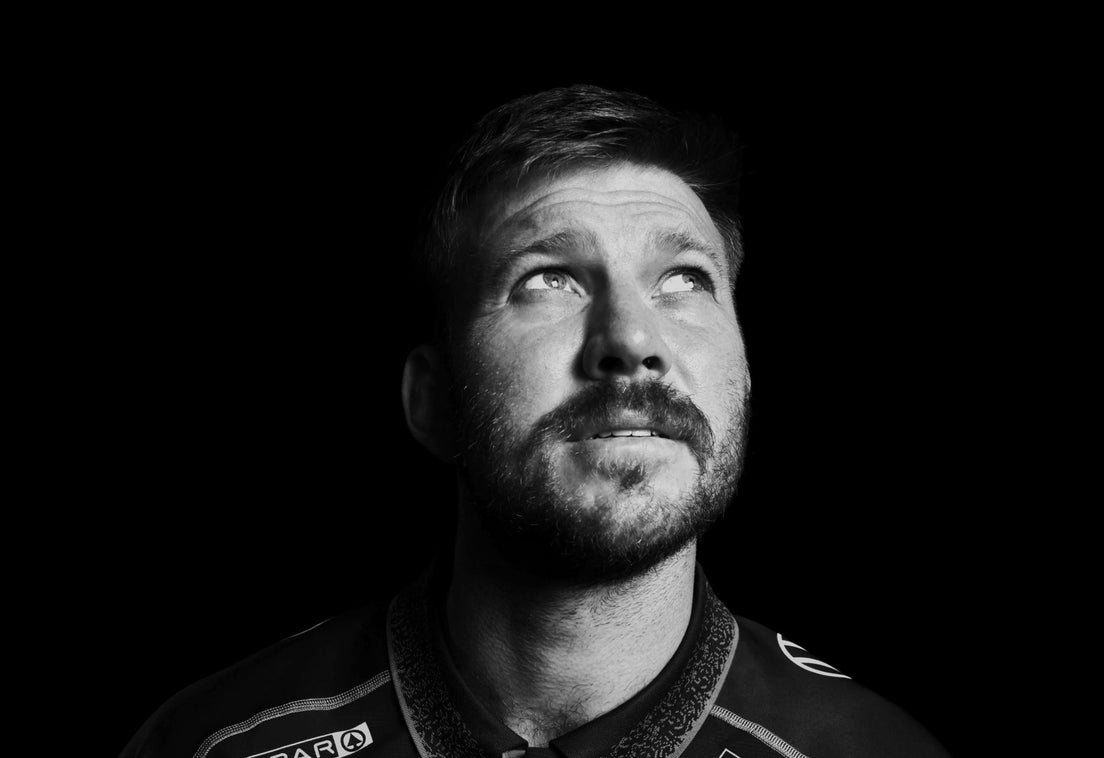 Black and white studio portrait of Stephan Lewies in the Sharks jersey, looking upwards against a black background.
