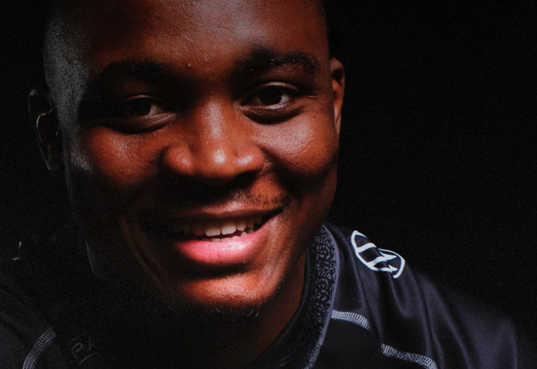 Low-key studio portrait of a smiling Hollywoodbets Sharks player in a black jersey, lit from the side against a black background.
