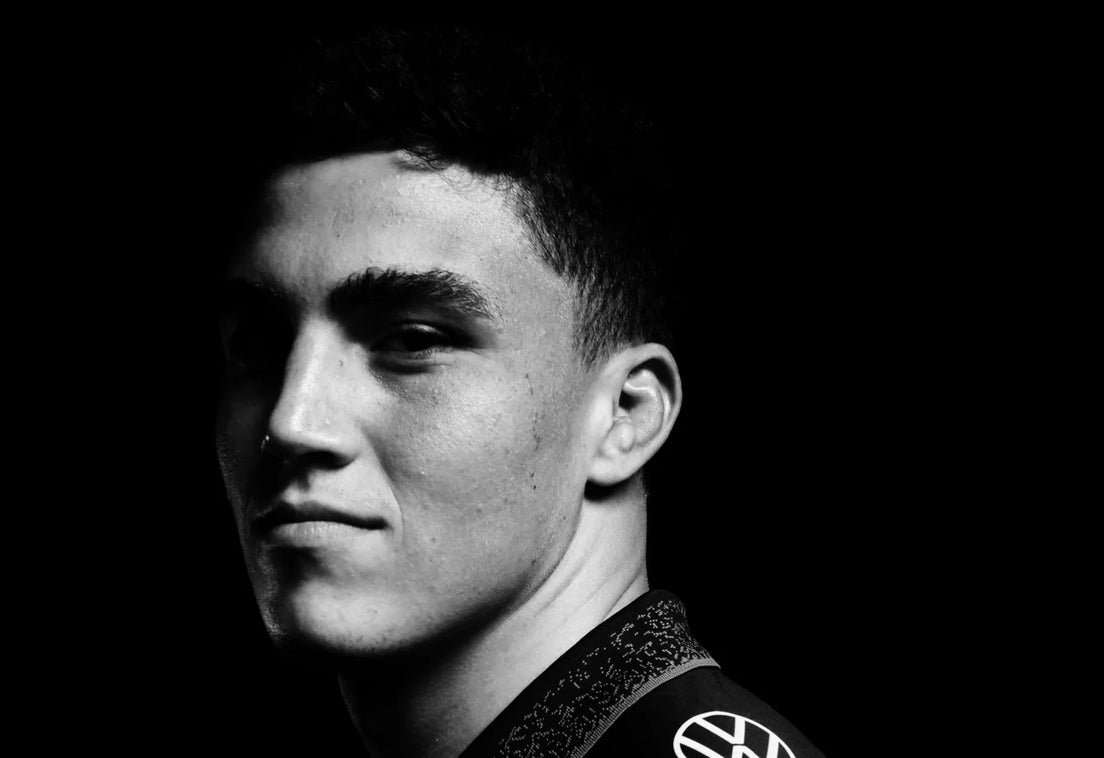 A Sharks player in the black jersey looks back over his shoulder at the camera in a black and white studio portrait against a black background.