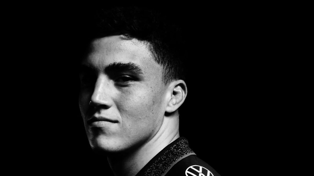 A Sharks player in the black jersey looks back over his shoulder at the camera in a black and white studio portrait against a black background.