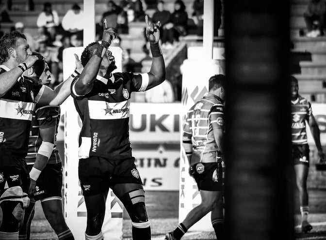 Hollywoodbets Sharks XV players celebrate a try, arms raised, in front of the advertising boards.
